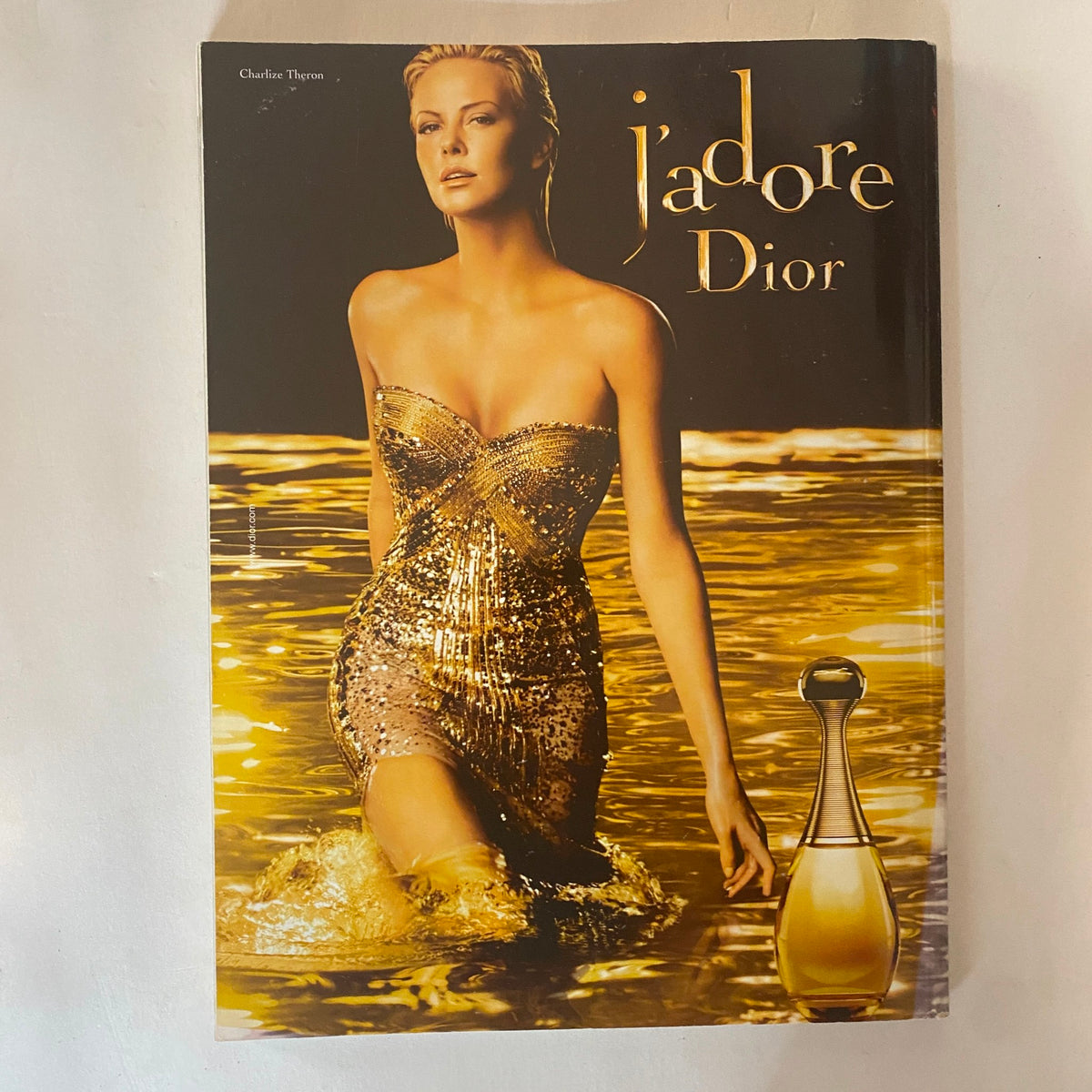 Cover of a 1990s Dior advertisement featuring a model in a golden dress, promoting the fragrance 'J'adore Dior'.
