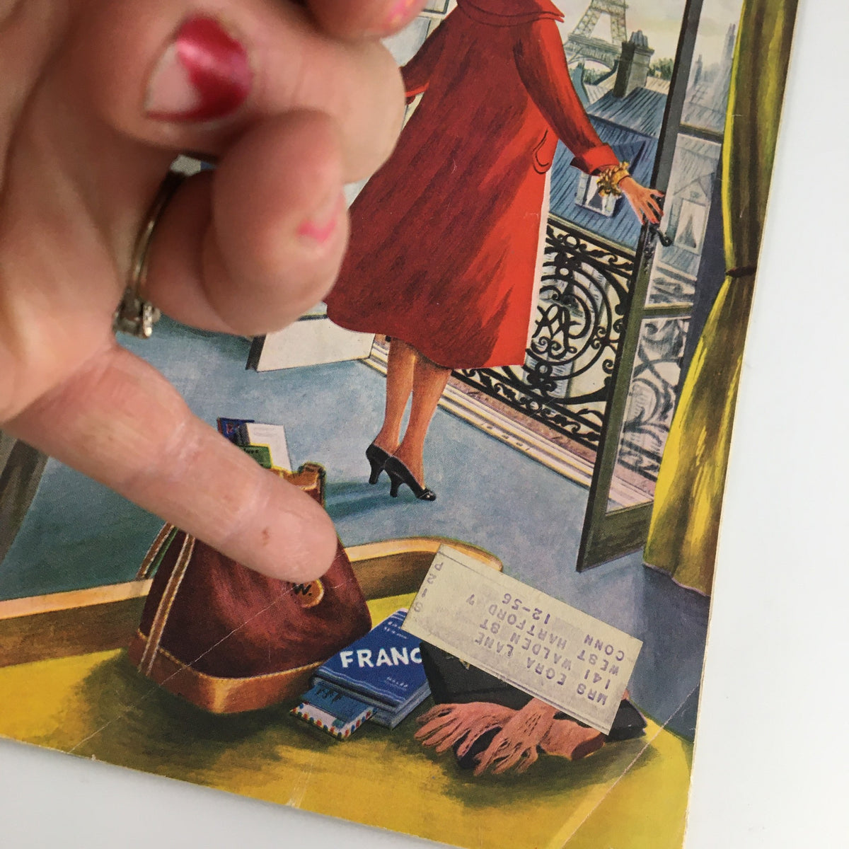 Detail of The Saturday Evening Post July 14 1956 magazine featuring TV's John Daly and Lucille Ball. A close-up view showing a hand pointing at the magazine cover with a woman in a red coat standing by a balcony adorned with Parisian architecture.