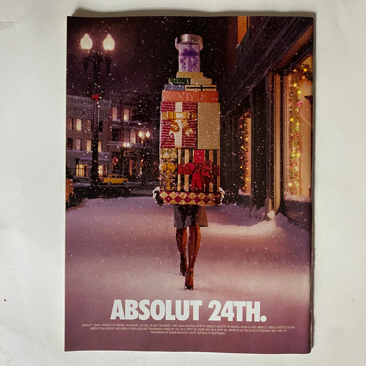 Advertisement from December 2000 showcasing a festive scene with a model carrying a stack of gifts, titled 'ABSOLUT 24TH'.