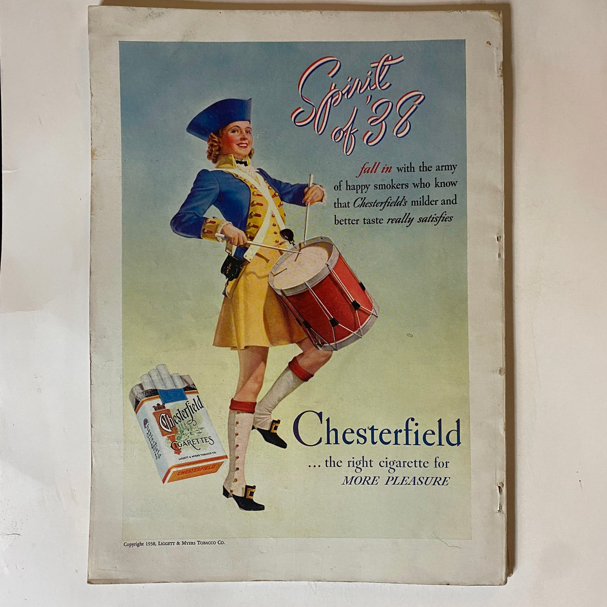 Advertisement from VTG The American Magazine July 1938 for Chesterfield cigarettes, featuring a marching band member in a colorful uniform promoting the product.
