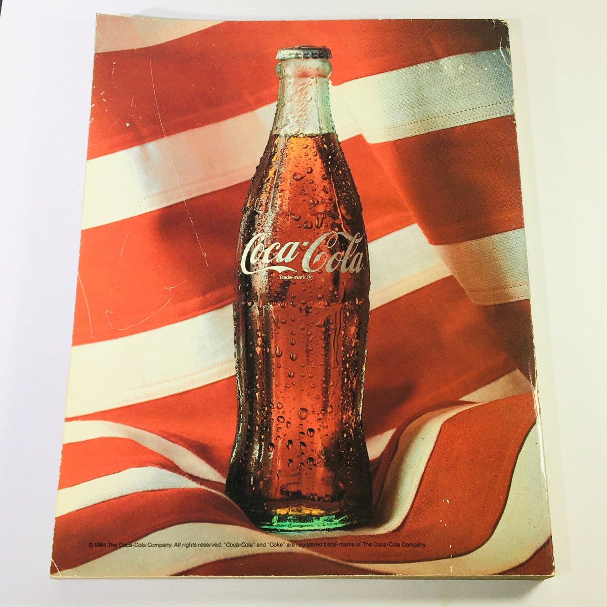 Cover page of the Official Olympic Souvenir Program 1984 - Games of XXIIIrd Olympiad Los Angeles depicting a retro Coca-Cola bottle against an American flag background.