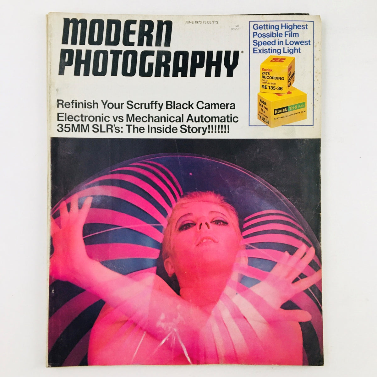 Cover of Modern Photography Magazine June 1973 featuring a bold graphic design and the headline 'Refinish Your Scruffy Black Camera Electronic vs Mechanical Automatic 35MM SLR's: The Inside Story!!!!!!' with a striking image of a model against a pink and black striped background.