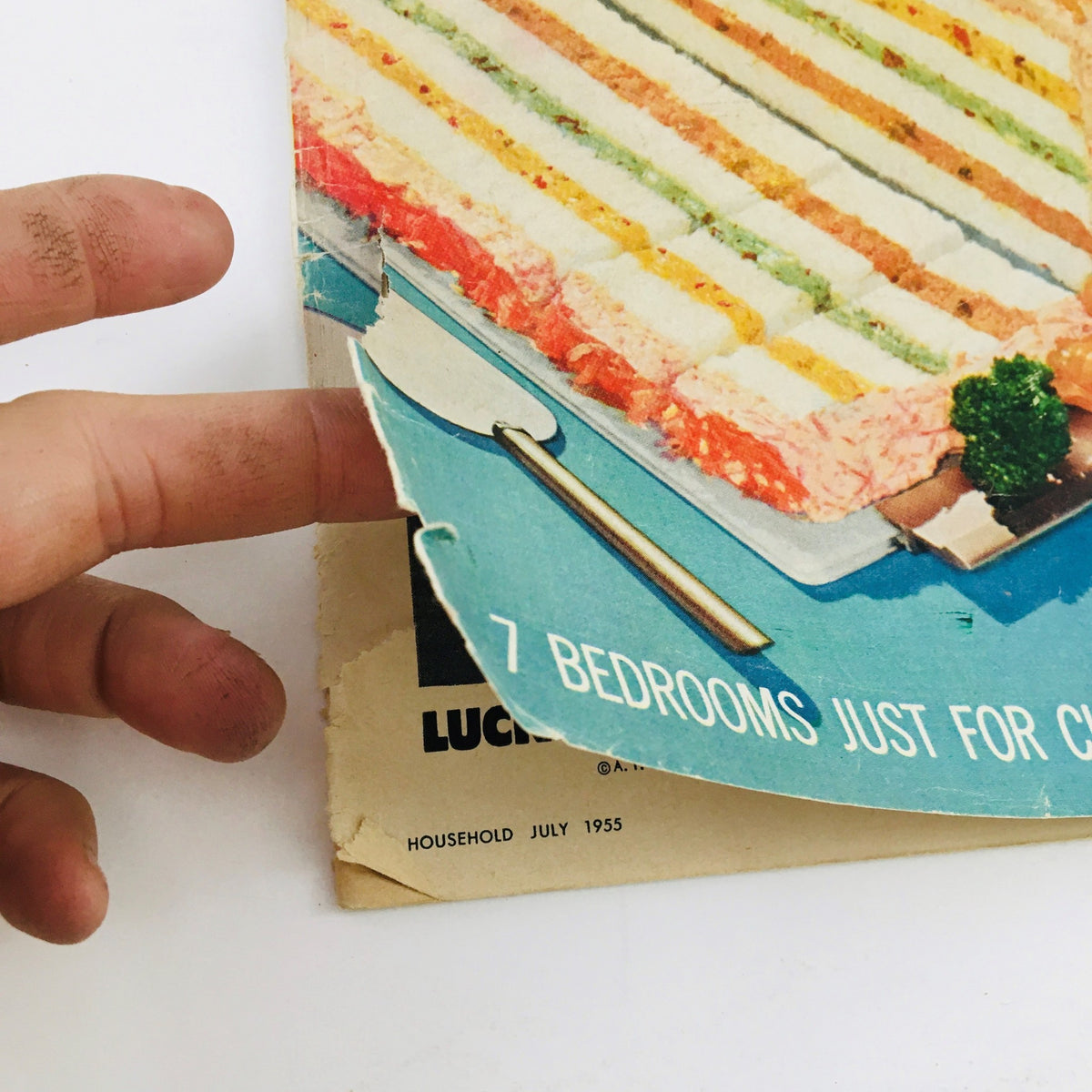 Close-up of the cover of Household Magazine July 1955 with a hand pointing at the layered sandwich and caption about children's bedrooms.