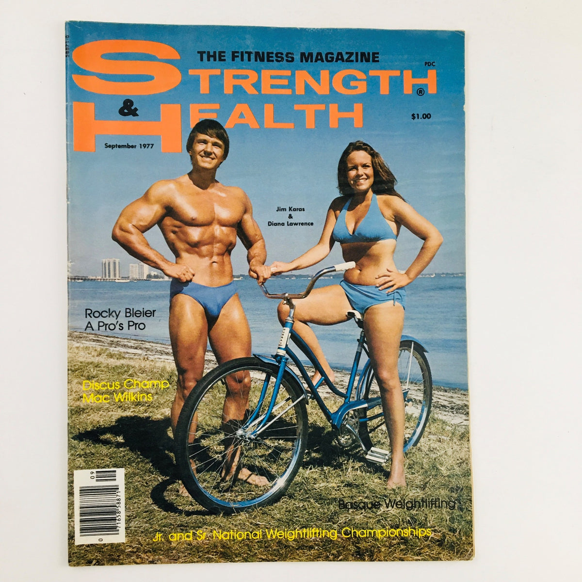 Cover of Strength & Health Magazine September 1977 featuring fitness icons Jim Karas and Diana Lawrence on the beach with a bicycle.
