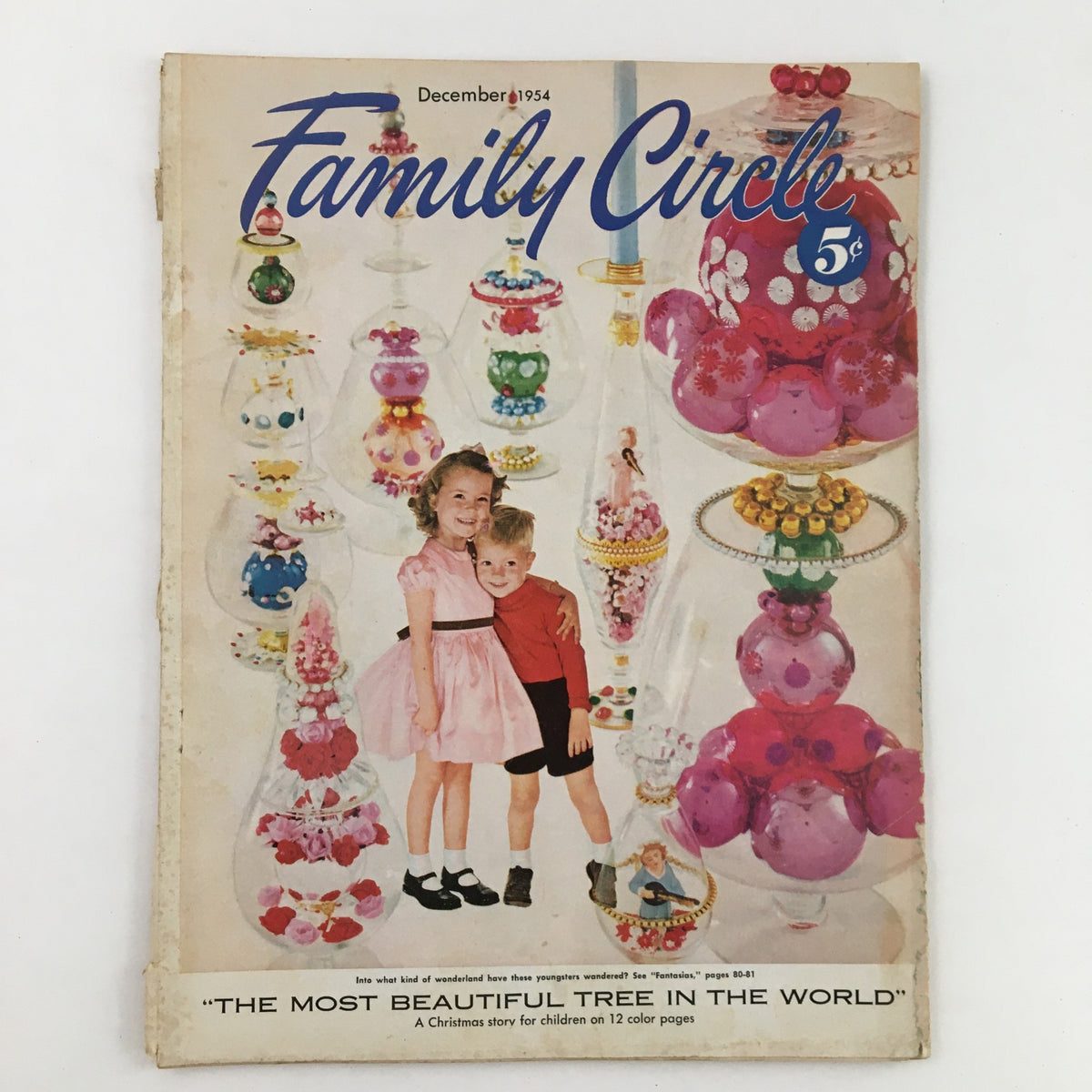 Cover of Family Circle Magazine from December 1954 featuring the title 'The Most Beautiful Tree in the World'. The cover showcases two children, a girl in a pink dress and a boy in black shorts, standing together amidst colorful decorative Christmas items.