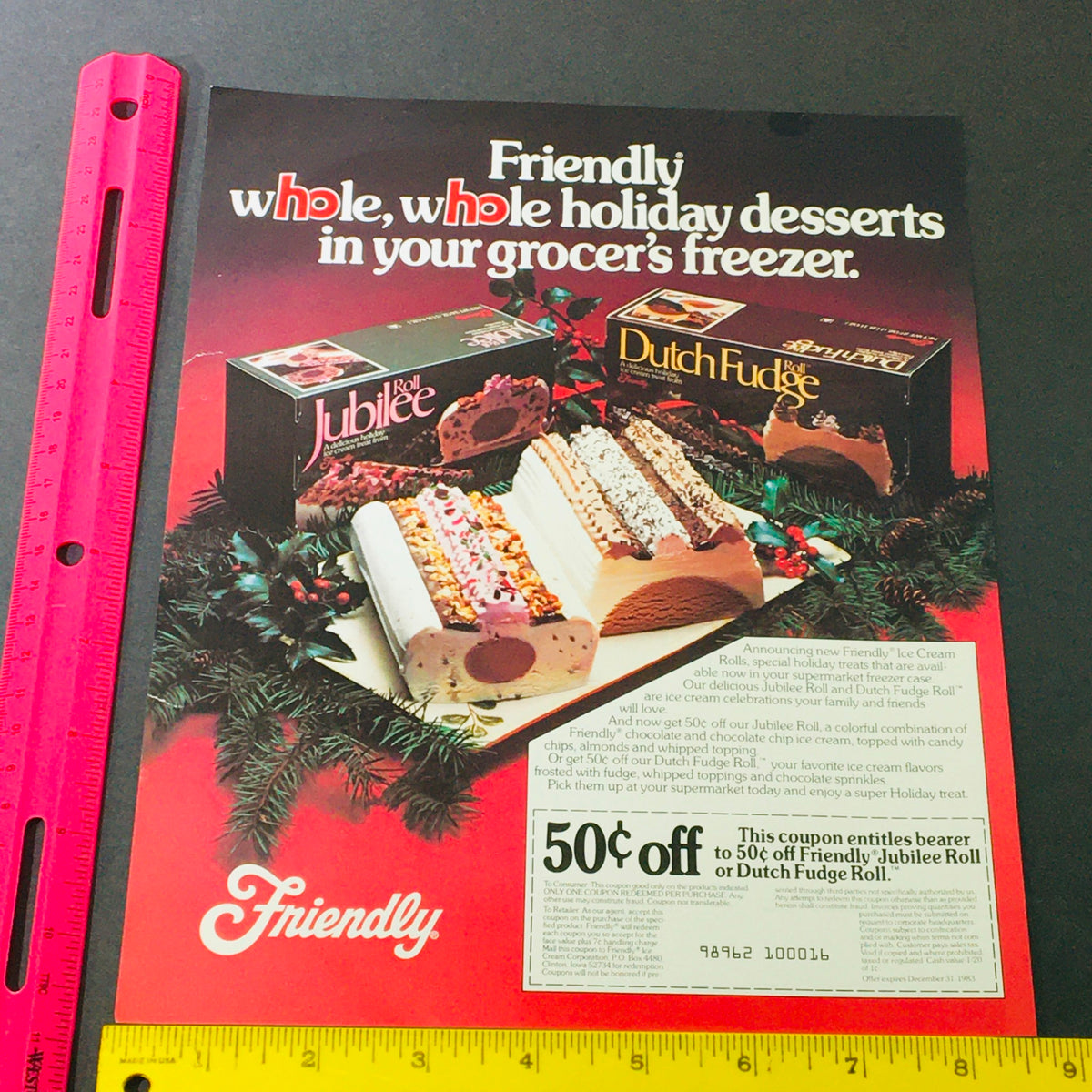Close-up view of the VTG Retro 1983 Friendly Jubilee Roll or Dutch Fudge Roll Desserts Ad Coupon measuring with a ruler, emphasizing the promotional offer and festive dessert imagery.