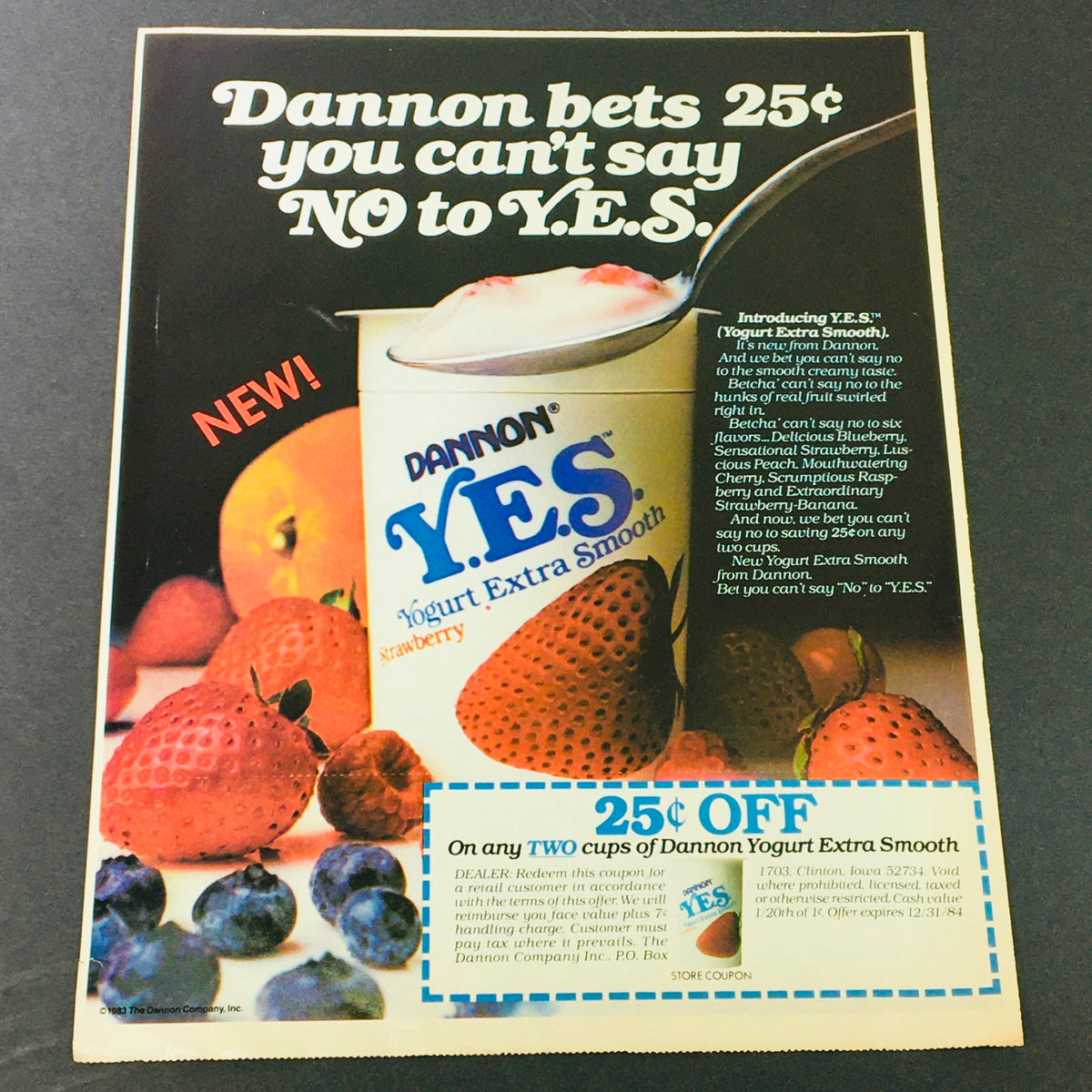 Dannon's vintage ad from 1983 featuring the new Y.E.S. (Yogurt Extra Smooth) product, offering a 25 cents discount on any two cups, surrounded by fresh fruits, promoting the smooth texture and flavors of the yogurt.
