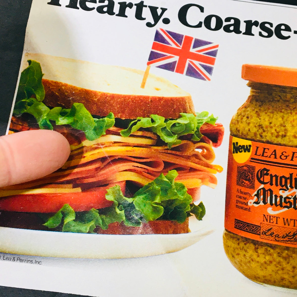 Close-up image of a sandwich topped with lettuce and a British flag, alongside a jar of Lea & Perrins English Pub Mustard in a vintage advertisement related to the 1983 Kellogg's Frosted Flakes Mattel Prize Vault Game.