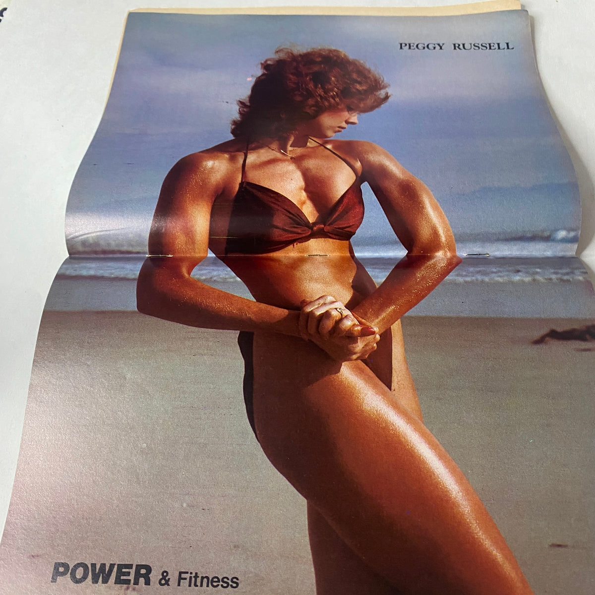 Centerfold from Power & Fitness for Everybody May 1981 featuring Peggy Russell, showcasing her muscular physique against a beach backdrop.