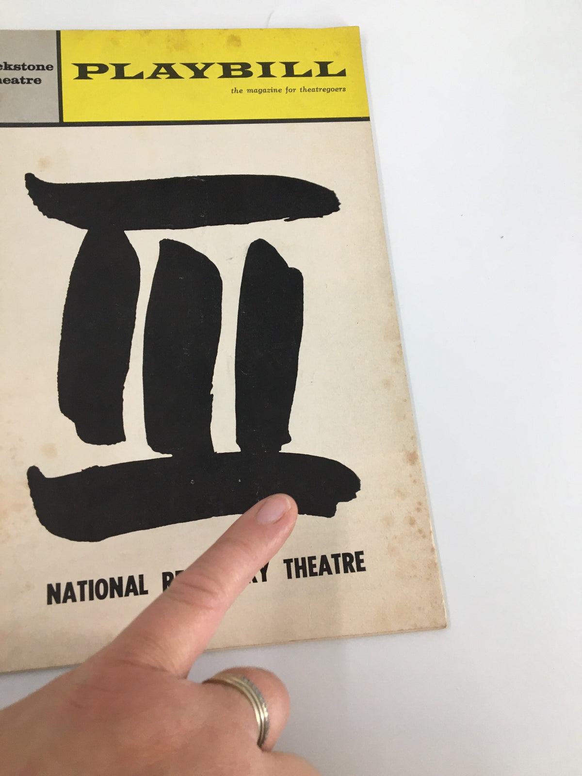 Close-up of the 1965 Playbill from the National Repertory Theatre, highlighting the cover with a finger pointing at the iconic black ink design.