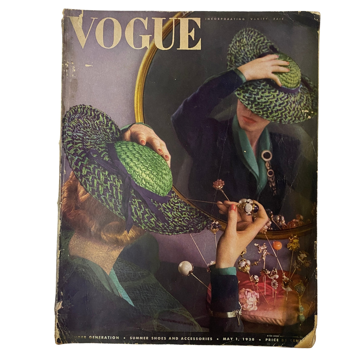 Vogue Magazine May 1, 1938 Cover featuring a woman in a green and purple hat, elegantly admiring herself in a mirror while surrounded by floral accessories. This vintage magazine represents fashion trends of the era, showcasing the artistry of Anton Bruehl.