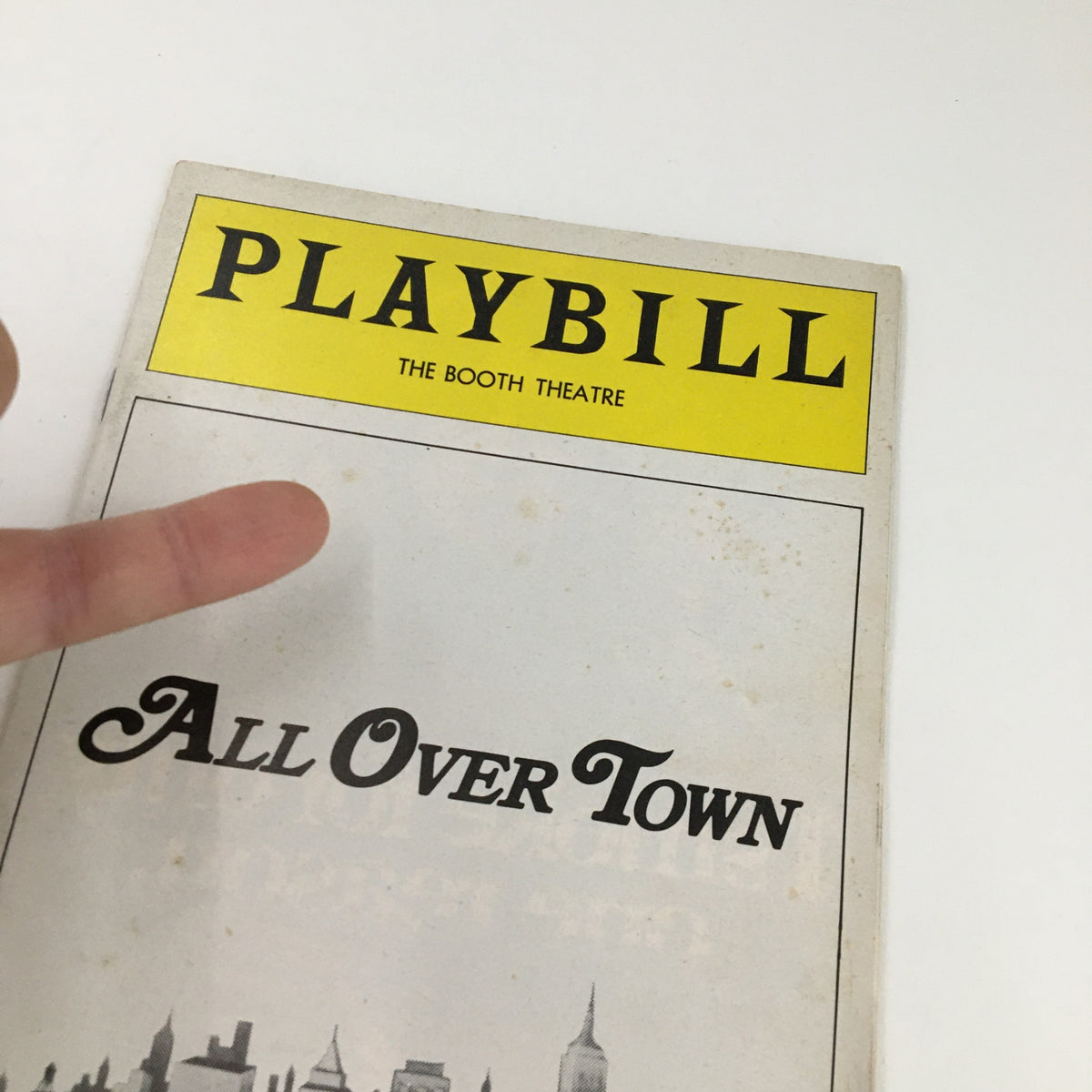 Close-up view of the 1975 Playbill for The Booth Theatre, highlighting the title 'All Over Town' with a person's finger pointing at it.