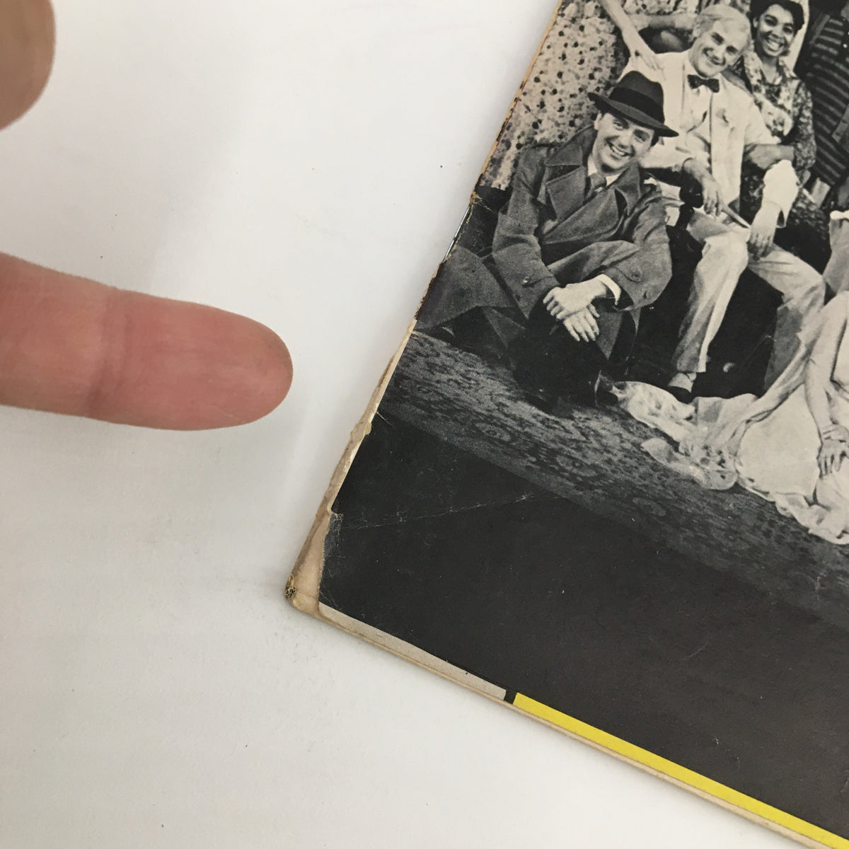 Close-up view of the edge of the 1966 Playbill for You Can't Take It With You, highlighting signs of wear at the binding and a person's finger pointing to the damaged area.