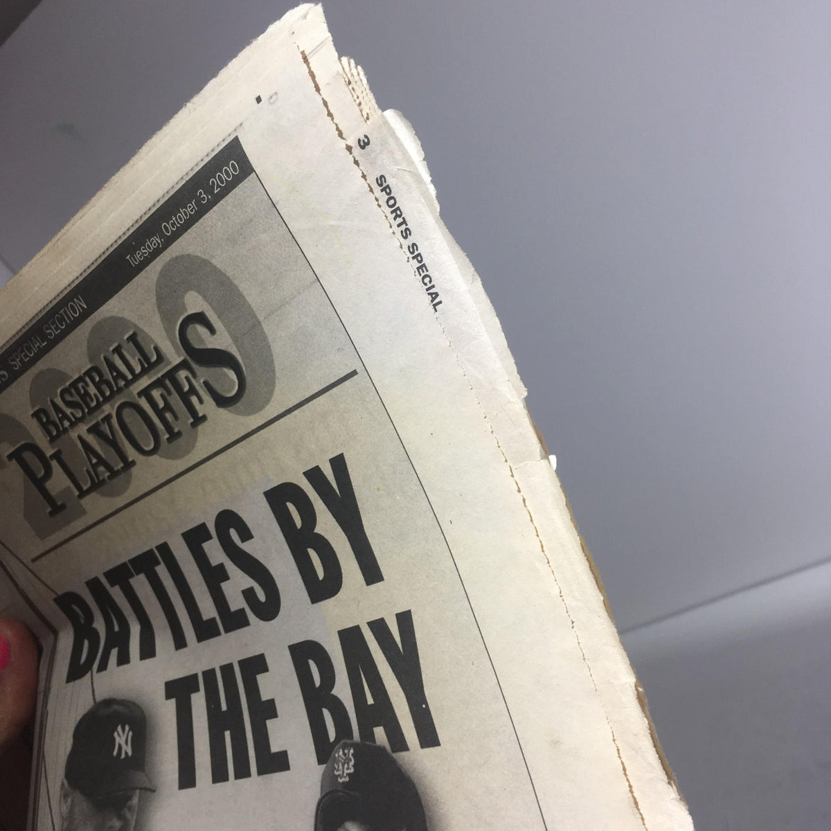 Close-up of the edge of a newspaper featuring the title 'NY Daily News: Oct 3 2000 Battles By The Bay Special', showcasing mild wear and a sports section header.