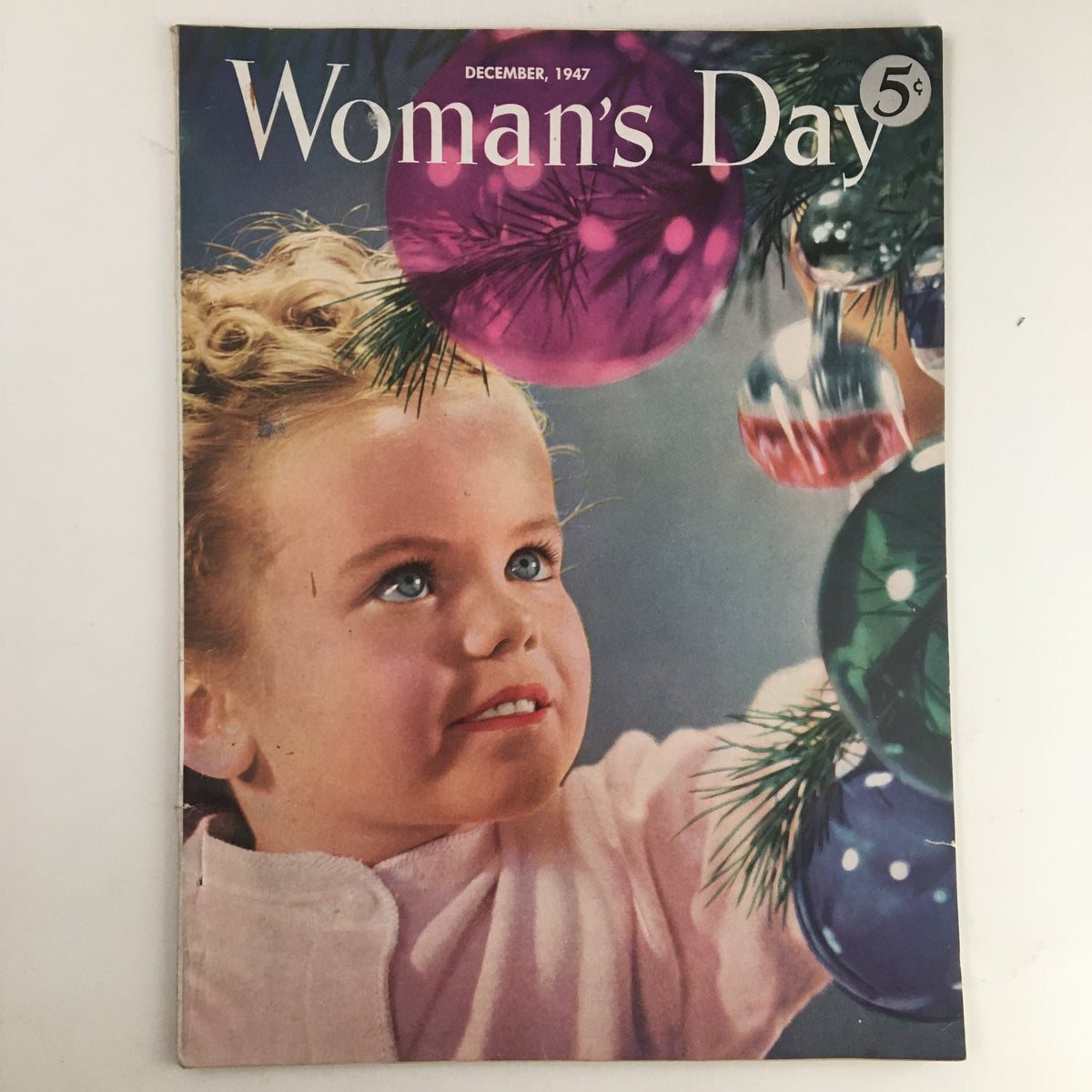 Cover of Woman's Day Magazine December 1947 featuring a young girl admiring colorful Christmas ornaments on a tree, embodying the festive spirit of holiday celebrations.