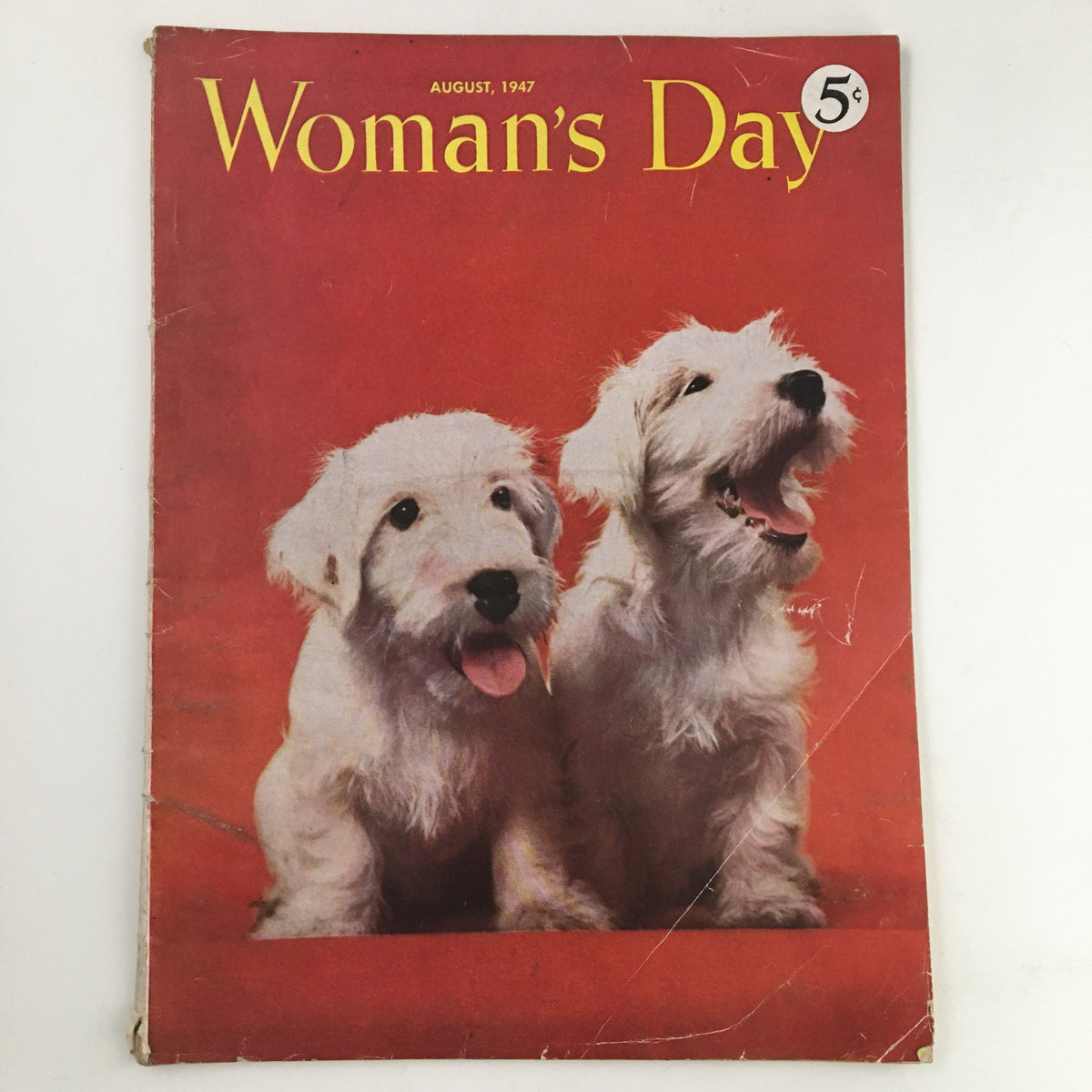 Cover of Woman's Day Magazine from August 1947 featuring two playful dogs on a red background, showcasing vintage American culture and post-war glamour.