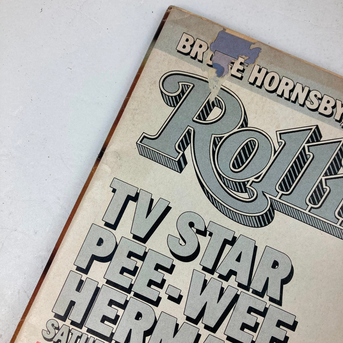 Close-up of the cover of Vintage Rolling Stone Magazine February 12 1987 Issue 493 featuring Pee-Wee Herman, highlighting a small tear and the magazine title.