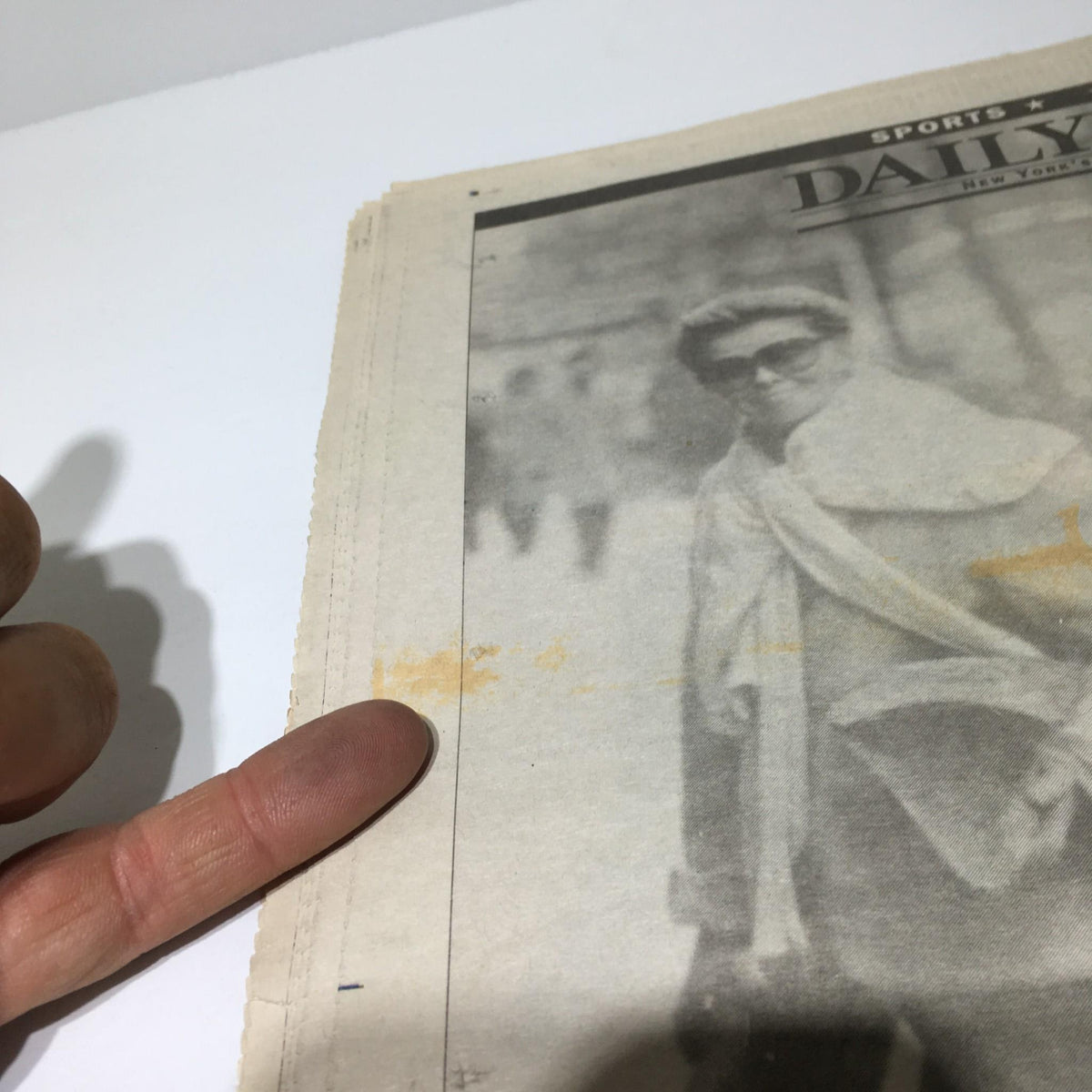Highlighted detail of NY Daily News from June 30, 2003, showing an individual's finger pointing to an old newsprint photo.