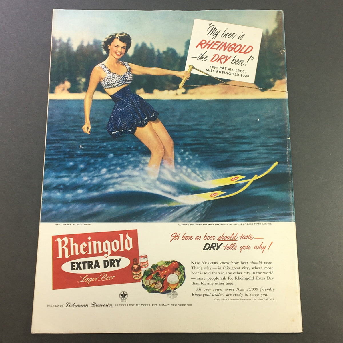 Advertisement for Rheingold Extra Dry Lager Beer, showcasing Miss Rheingold 1949 water skiing in a vintage swimsuit with a scenic background.