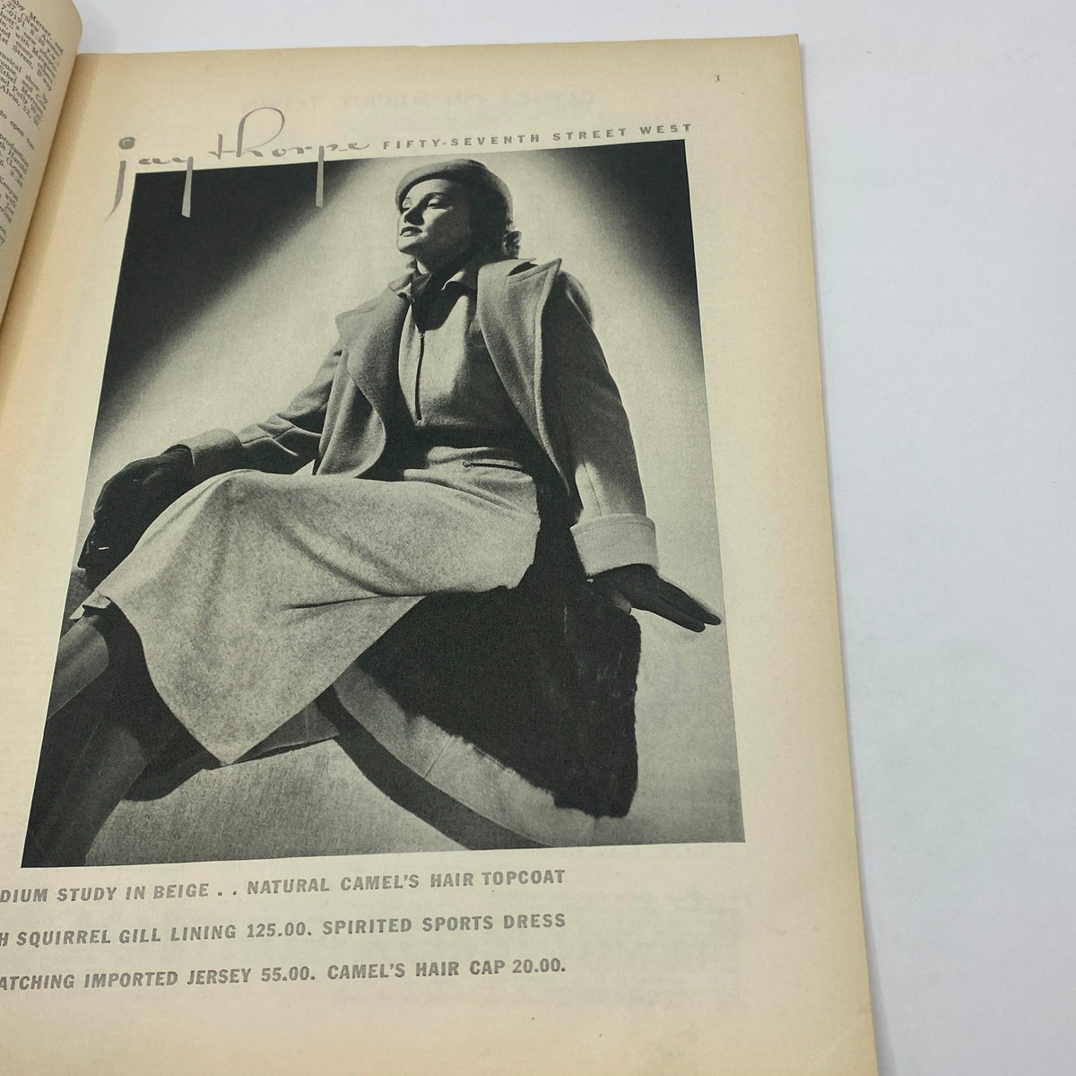 Fashion advertisement from The New Yorker magazine, October 24, 1936, showcasing a model in a beige camel's hair topcoat, highlighting classic styles of the 1930s.
