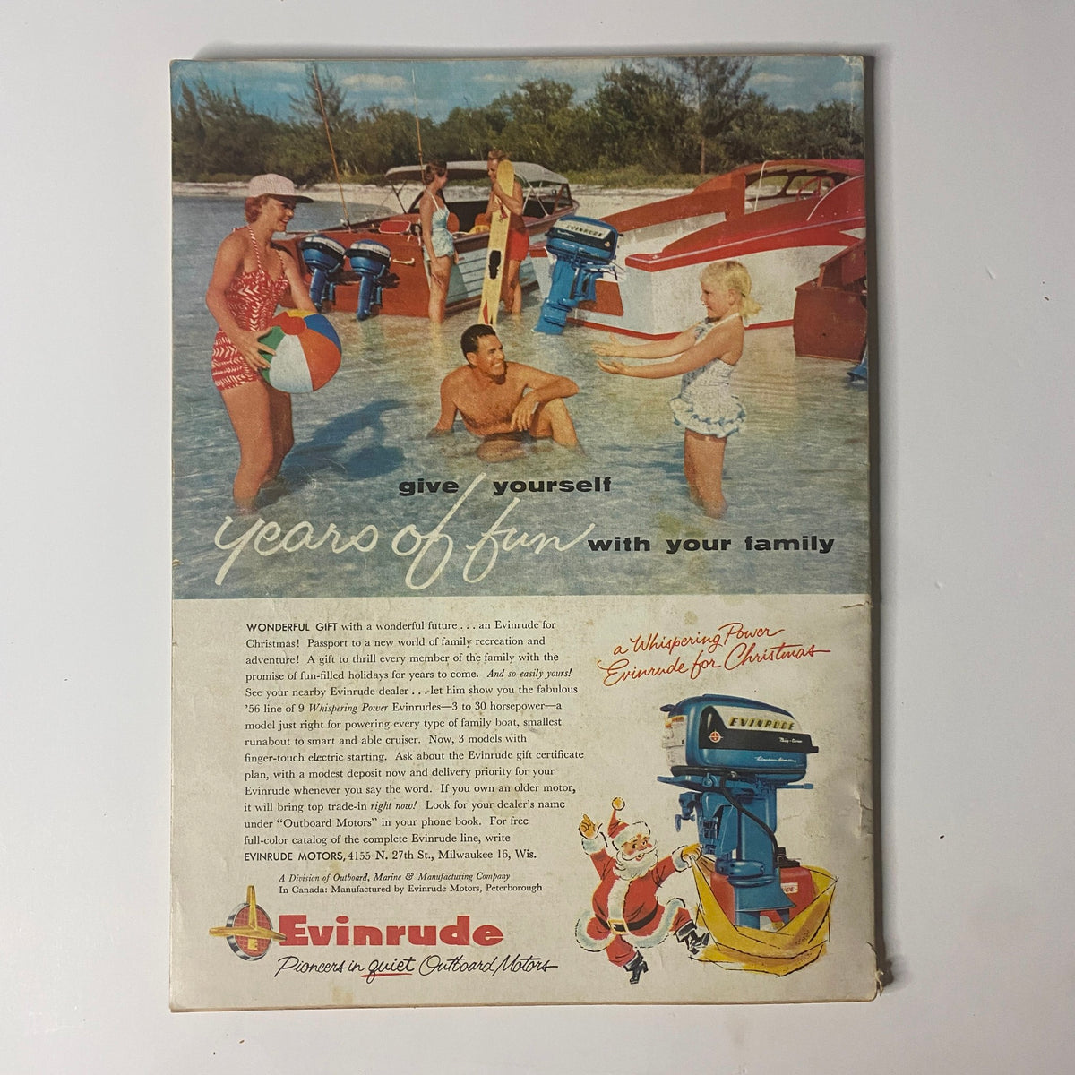 Back cover of Outdoor Life Magazine, December 1955, showcasing a vintage advertisement for Evinrude motors, depicting families enjoying beach activities with boats.