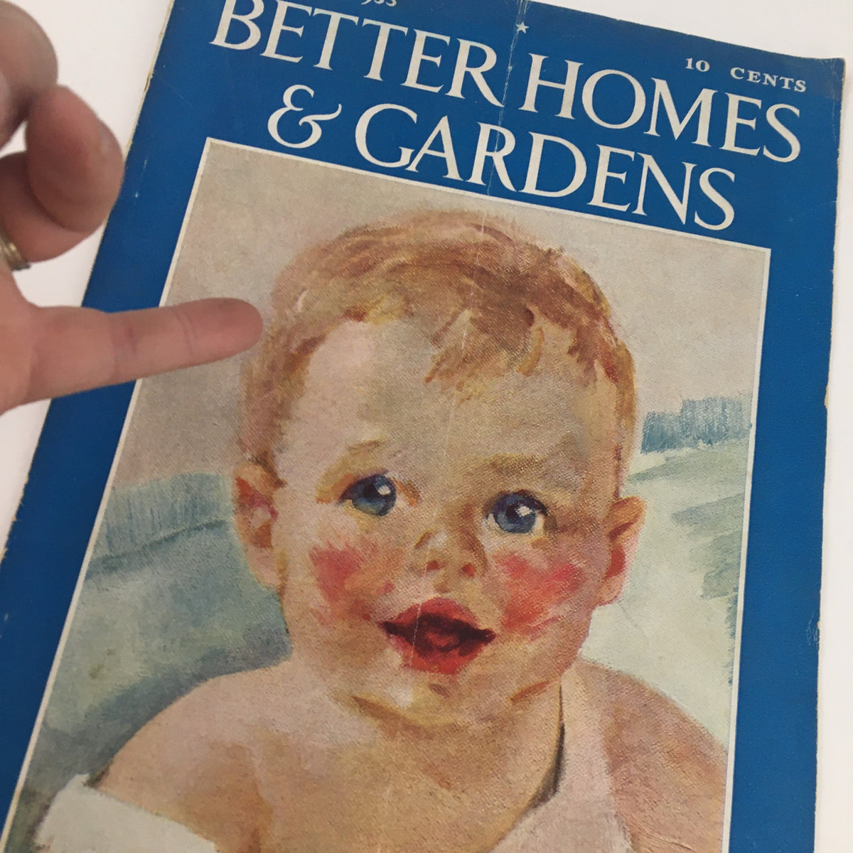 Close-up of the cover of Better Homes & Gardens Magazine January 1933, highlighting the baby illustration and the magazine title in blue. A hand is pointing at the cover.