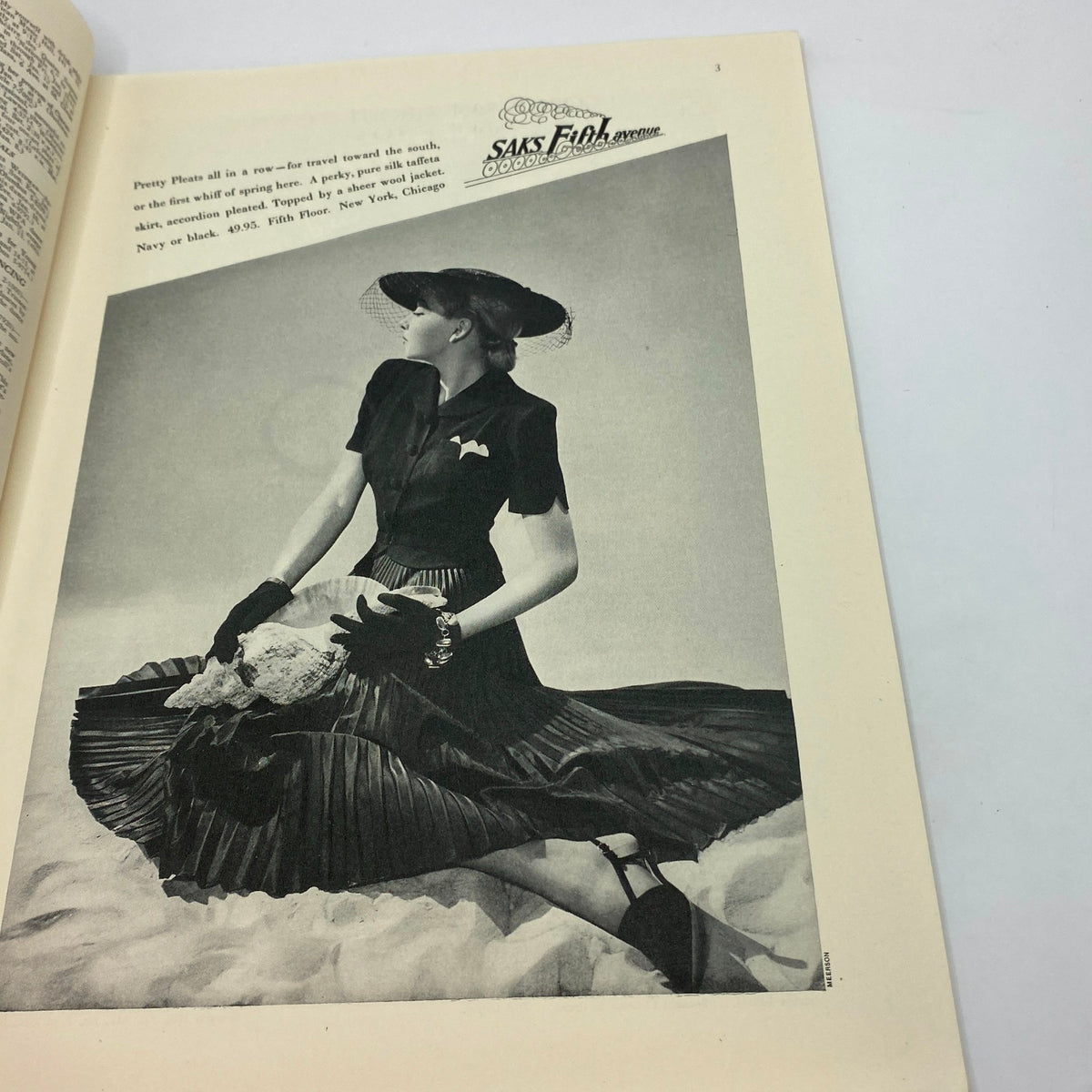Vintage fashion advertisement from The New Yorker, January 8, 1938, featuring a model in a black pleated skirt holding a seashell, showcasing the elegance and style of the late 1930s.