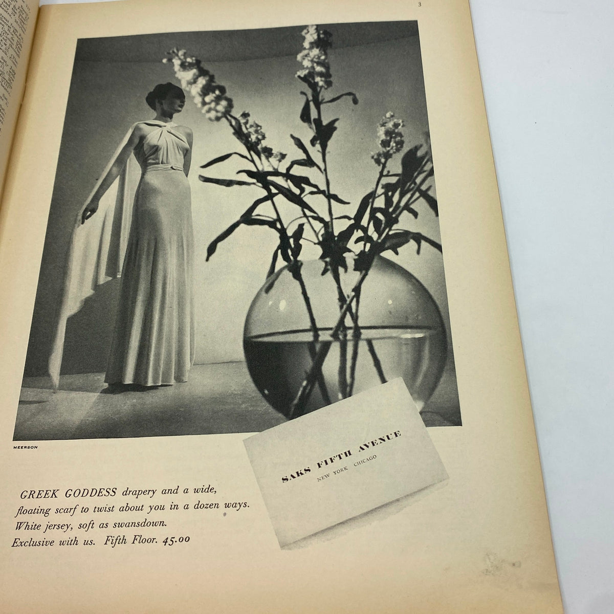 Fashion advertisement from The New Yorker Complete Magazine July 24, 1937 showcasing a model in a white gown labeled 'Greek Goddess' with a flower arrangement.