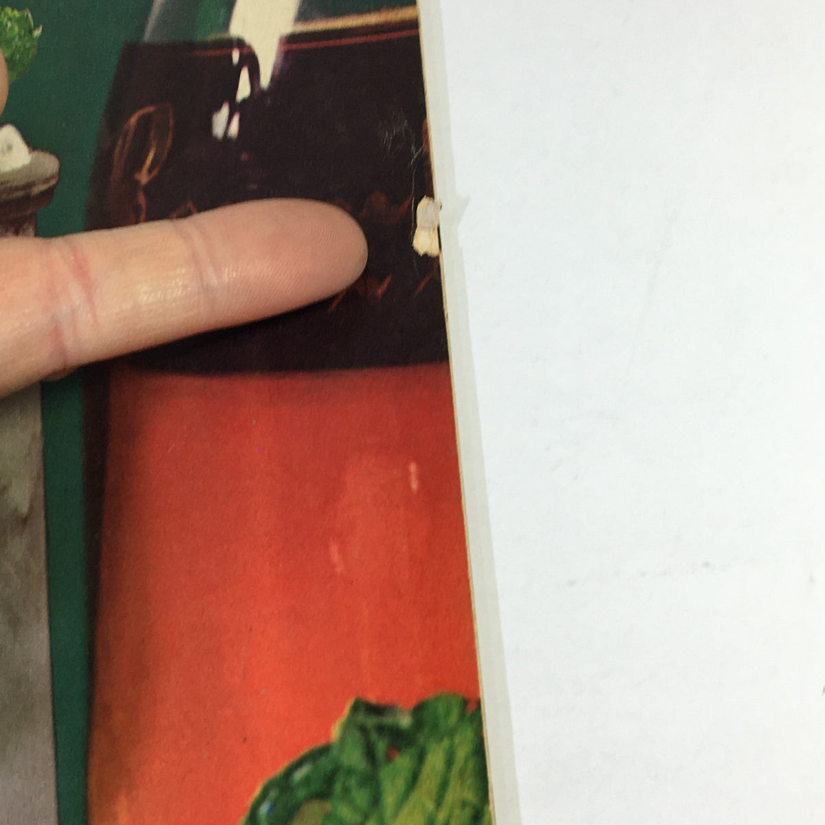 Close-up view of VTG Gourmet The Magazine of Good Living July 1968 displaying wear and tear, including a small tear and finger pointing towards a colorful image related to a wine tour of France.