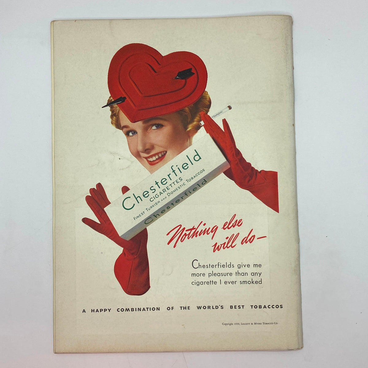 Charming vintage Chesterfield cigarette advertisement featuring a smiling woman wearing a heart-shaped red hat and red gloves. The ad includes the tagline 'Nothing else will do' and highlights Chesterfield's quality as 'the world's best tobaccos'. Perfect for collectors of 1930s magazine art and advertising.
