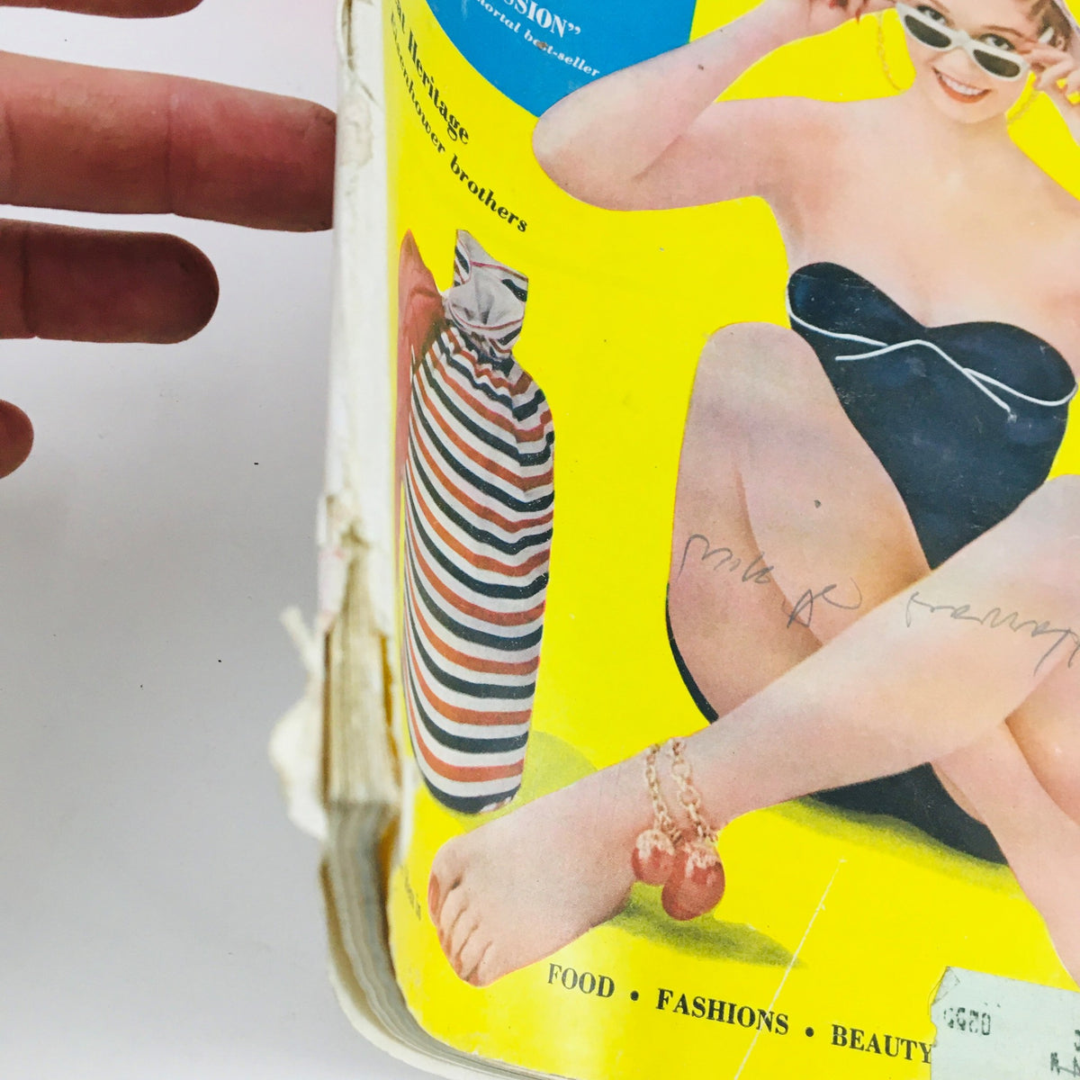 Close-up view of the Woman's Home Companion August 1954 magazine cover showing details of a woman's black swimsuit, sandals, and a striped beach bag.
