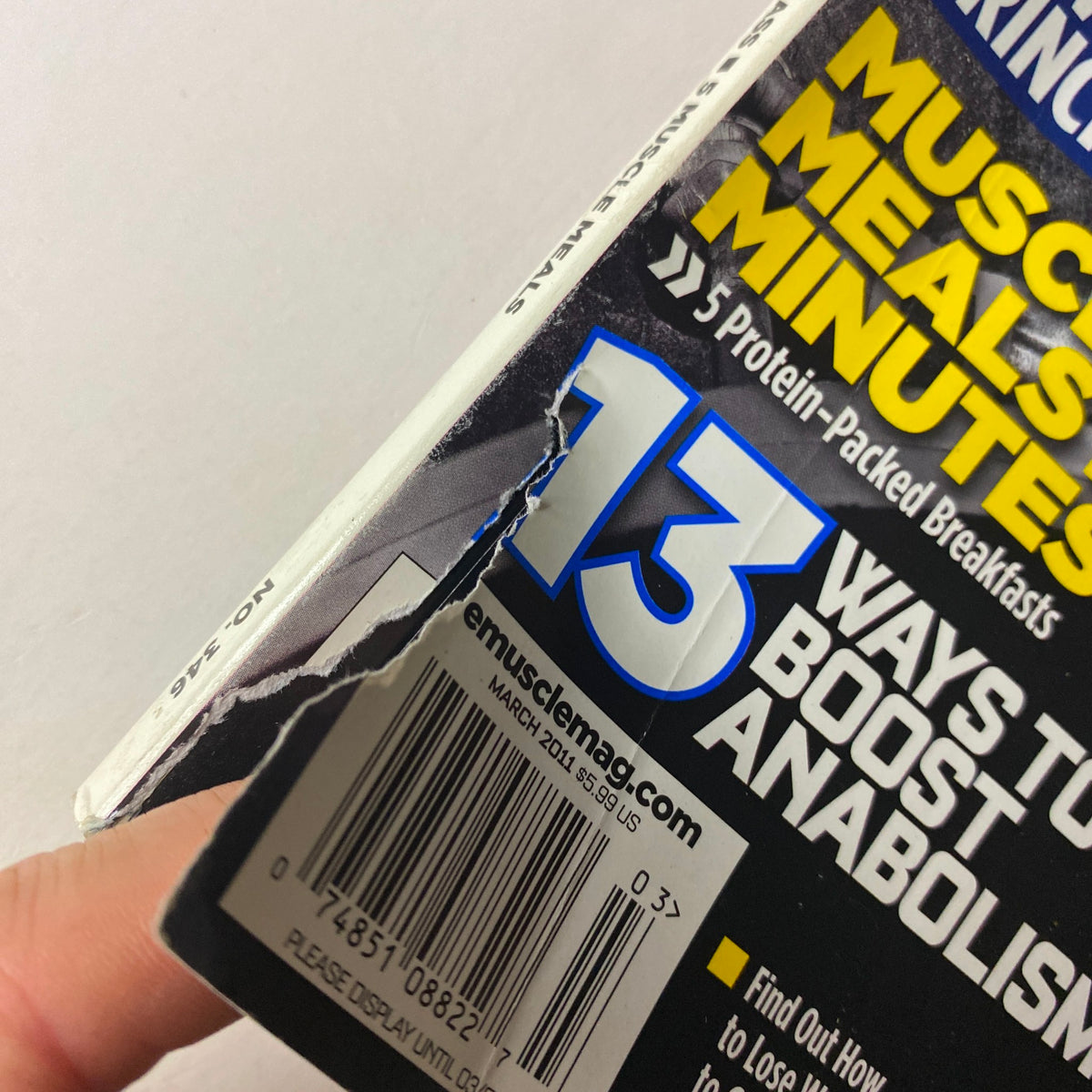 Close-up of the spine edge of MuscleMag International Magazine March 2011, No. 346 showing a damaged area and the publication date, highlighting its collectible nature.