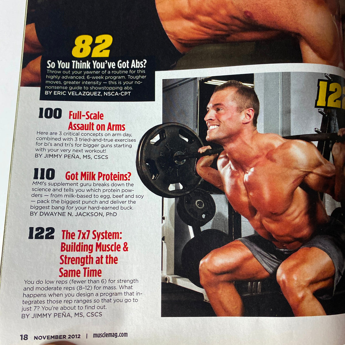 Interior page from MuscleMag International Magazine November 2012, highlighting articles including 'So You Think You've Got Abs?', 'Full-Scale Assault on Arms', and 'Got Milk Proteins?'. Features workout tips by Eric Velazquez, Jimmy Peña, and Dwayne N. Jackson.