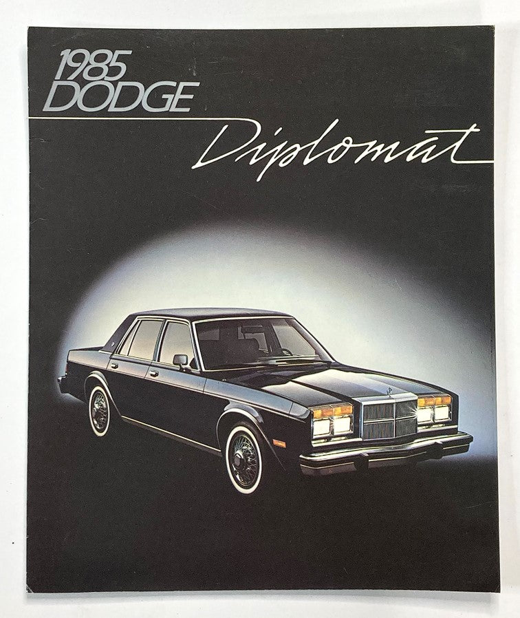 1985 Dodge Diplomat Dealer Showroom Sales Brochure Guide Catalog featuring a black 1985 Dodge Diplomat sedan displayed against a gradient background.