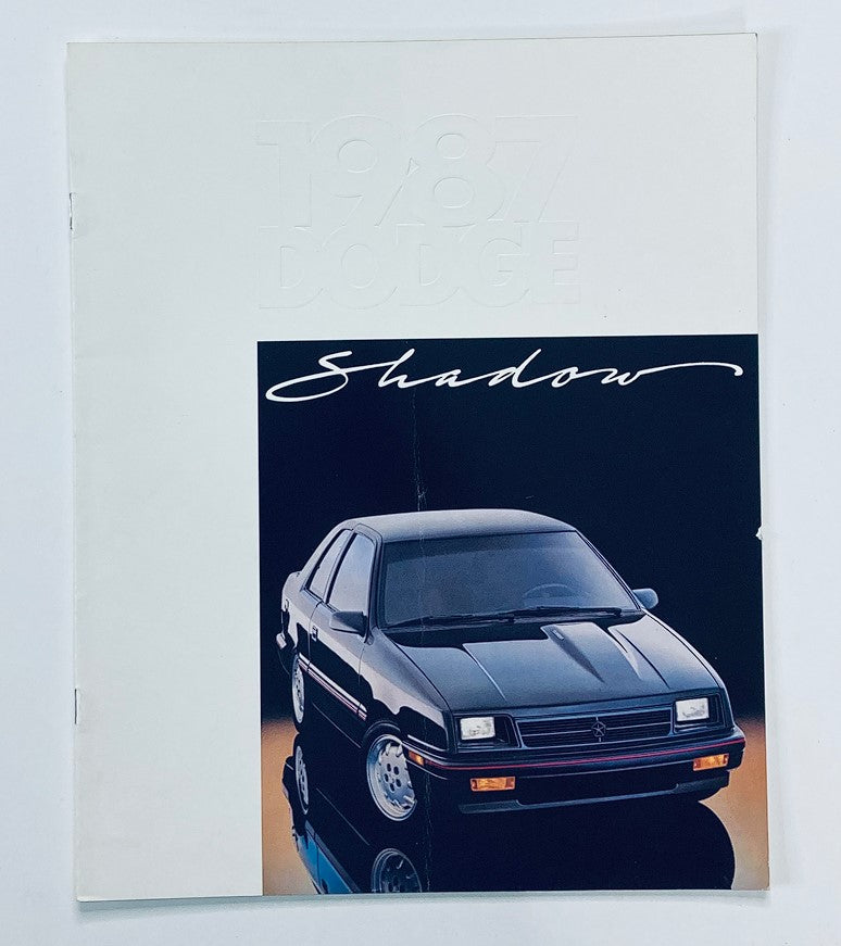 Cover of the 1987 Dodge Shadow Dealer Showroom Sales Brochure Guide Catalog featuring a sleek black Dodge Shadow car with a reflective background. This vintage brochure showcases the iconic vehicle of the late 1980s, highlighting its design and marketing.