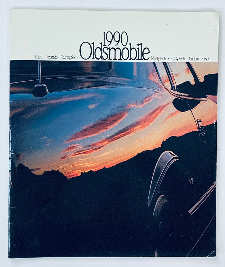 Cover of the 1990 Oldsmobile Touring Sedan Dealer Showroom Sales Brochure Guide Catalog featuring a scenic sunset reflection on the car's exterior.