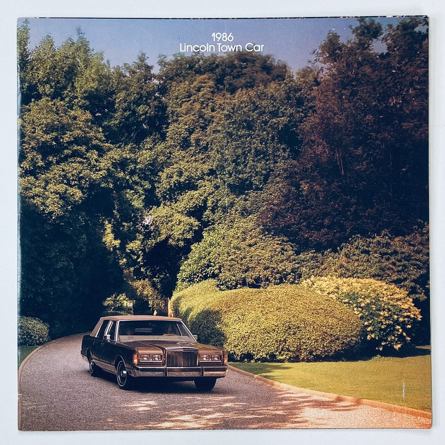 Cover of the 1986 Lincoln Town Car Dealer Showroom Sales Brochure Guide Catalog featuring a classic Lincoln Town Car parked on a scenic road surrounded by greenery.