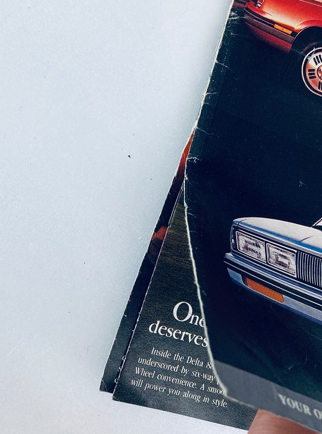 Close-up view of the 1980s Oldsmobile Lineup Dealer Showroom Sales Brochure, highlighting the wear of the brochure with elements of old photographs and textures.