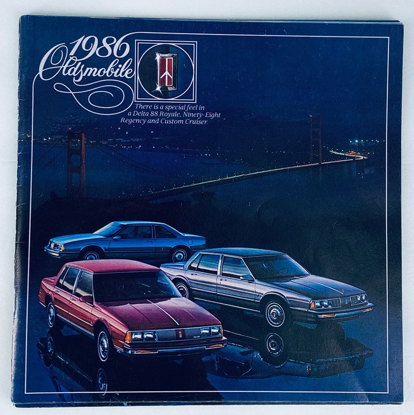 1986 Oldsmobile Lineup Dealer Showroom Sales Brochure Guide Catalog featuring a nighttime scene with three Oldsmobile cars: a Delta 88 Royale, a Ninety-Eight Regency, and a Custom Cruiser, set against a backdrop of a bridge.