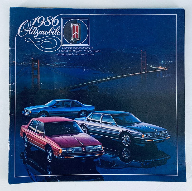 1986 Oldsmobile Delta 88 Royale Dealer Showroom Sales Brochure Guide Catalog featuring three Oldsmobile cars displayed in front of a nighttime backdrop of the Golden Gate Bridge.