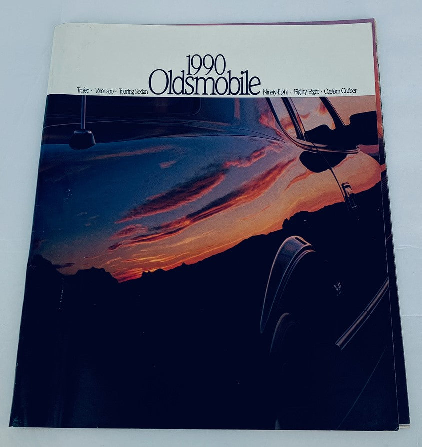 Cover of the 1990 Oldsmobile Touring Sedan Dealer Showroom Sales Brochure, featuring a scenic sunset reflection on a vehicle, showcasing the model's elegance.