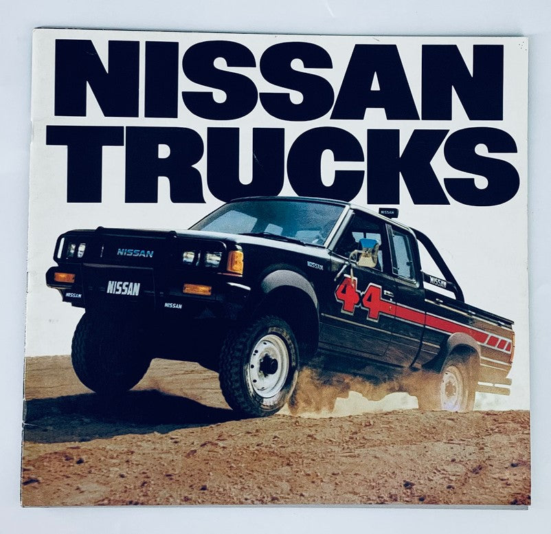 1984 Nissan Trucks Dealer Showroom Sales Brochure featuring a black Nissan truck with bold 'NISSAN TRUCKS' text and an off-road backdrop.