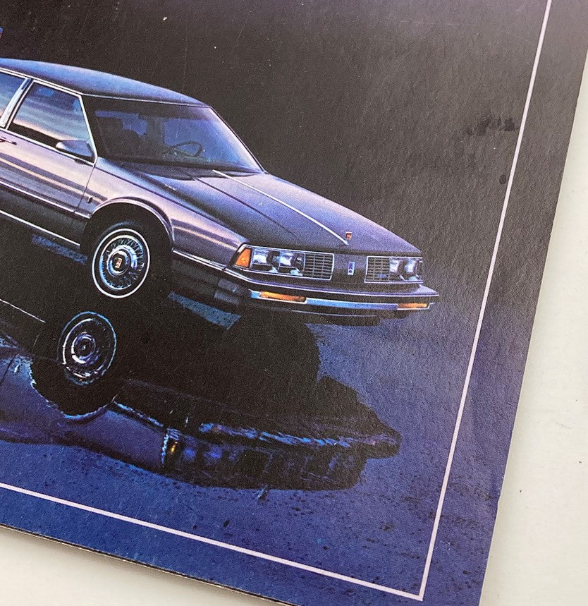 Close-up image of the 1986 Oldsmobile Delta 88 Royale showcased in the showroom sales brochure, highlighting its sleek design and reflective surface.