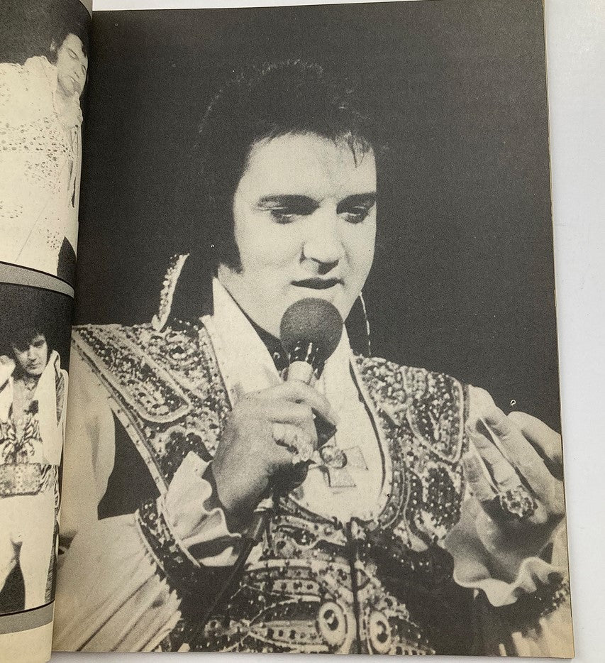 Black and white photo from 'The Real Elvis' magazine, showing Elvis Presley holding a microphone during a performance, reflecting his captivating stage presence.