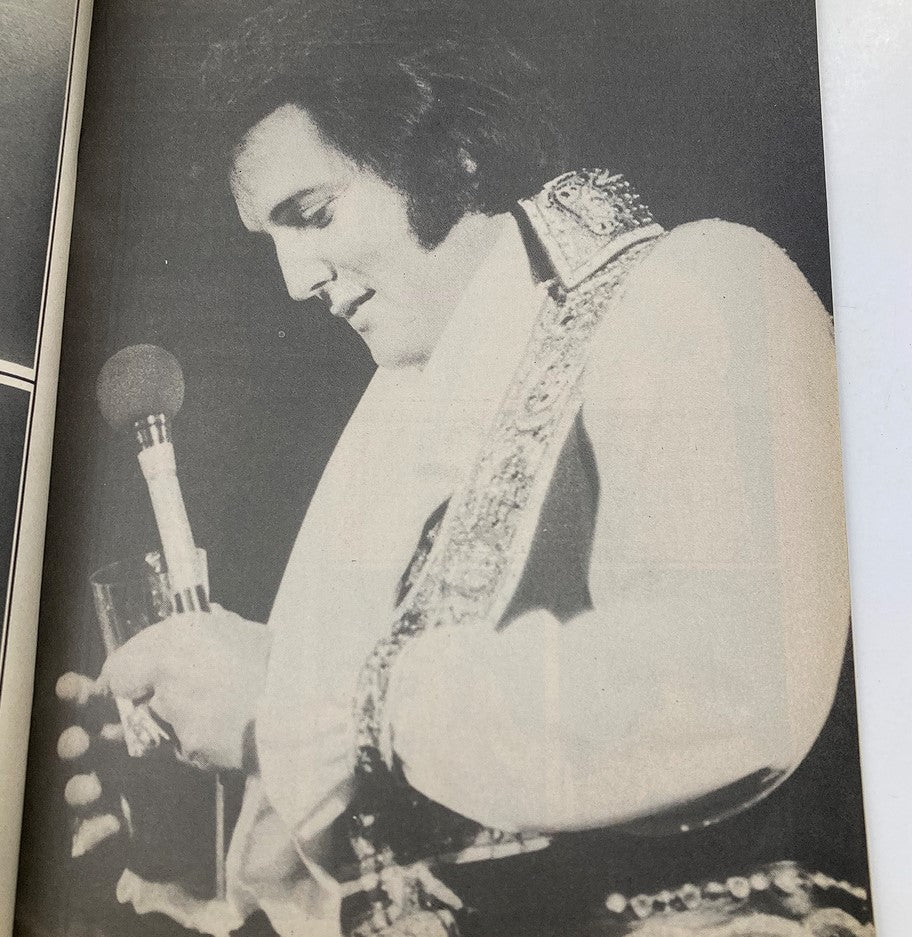 Black and white image from 'The Real Elvis' magazine, featuring Elvis Presley in a performance pose, holding a glass and microphone, emphasizing his charisma and showmanship.