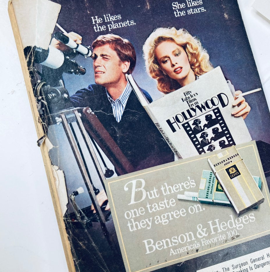 Vintage advertisement featuring a man looking through a telescope and a woman reading a magazine titled 'Hollywood.' The ad promotes Benson & Hedges cigarettes, highlighting a couple's shared preference for different interests. Related to the TV Guide Magazine dated September 21, 1985 featuring Michael J. Fox.