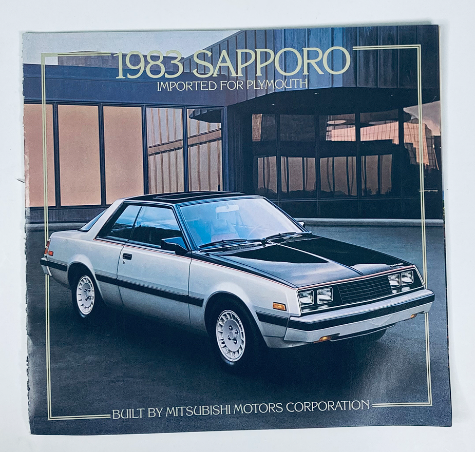 1983 Mitsubishi Sapporo Dealer Showroom Sales Brochure Guide Catalog featuring a stylish black and silver 1983 Sapporo car model in front of a modern building.