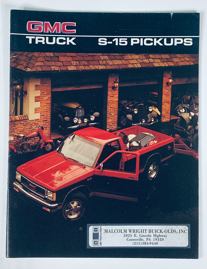 1986 GMC S-15 Pickups Dealer Showroom Sales Brochure featuring a red GMC S-15 pickup truck parked outside a dealership, showcasing the vehicle and its surroundings.