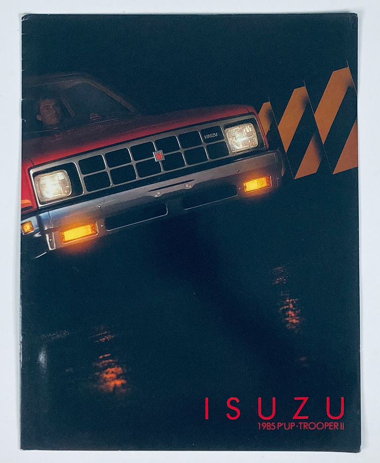 Cover of the 1985 Isuzu Pickup & Trooper II Dealer Showroom Sales Brochure featuring a red Isuzu vehicle in a stylish dark setting, showcasing the vintage automotive design.