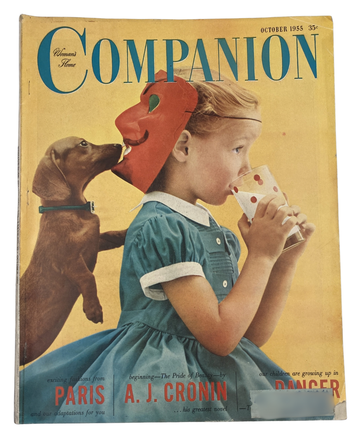 Cover of Woman’s Home Companion Magazine October 1955 featuring a little girl in a blue dress drinking a beverage, with a playful dog beside her, showcasing Paris fashion themes. By A. J. Cronin.